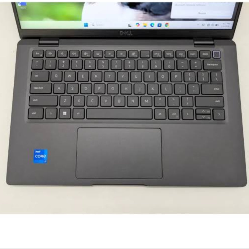 A dark gray Dell laptop with an open screen, showing a Windows desktop, photographed from a top-down angle on a light off-white surface.